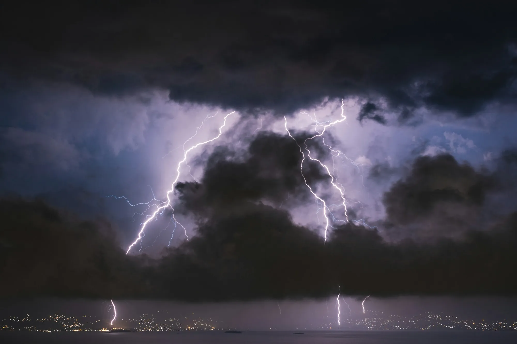 Lightning striking behind dark storm clouds over open country